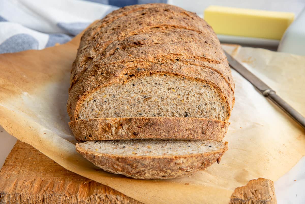 The Seed and Grain Sourdough Loaf is sliced on a sheet of browned parchment set on a wooden cutting board.