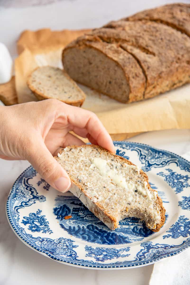A hand puts down a slice of Seed and Grain Sourdough Loaf with a bite taken from it.