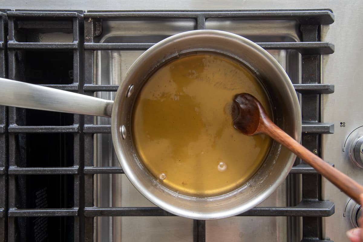 A wooden spoon is used to stir the concentrated simple syrup in a silver pot.