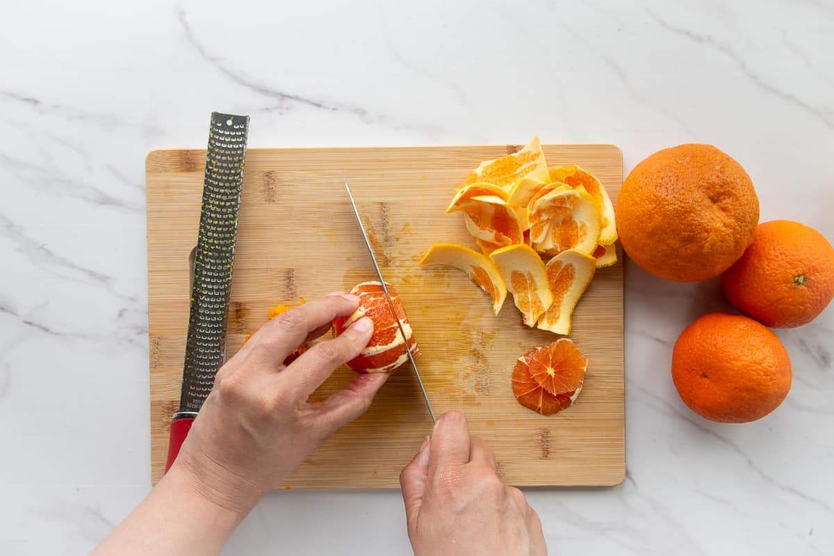 The citrus are peeled and sliced on a wooden cutting board.
