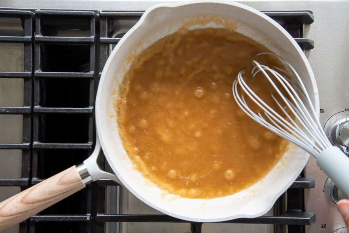 The butter and sugar caramel are whisked together in a grey sauce pan.