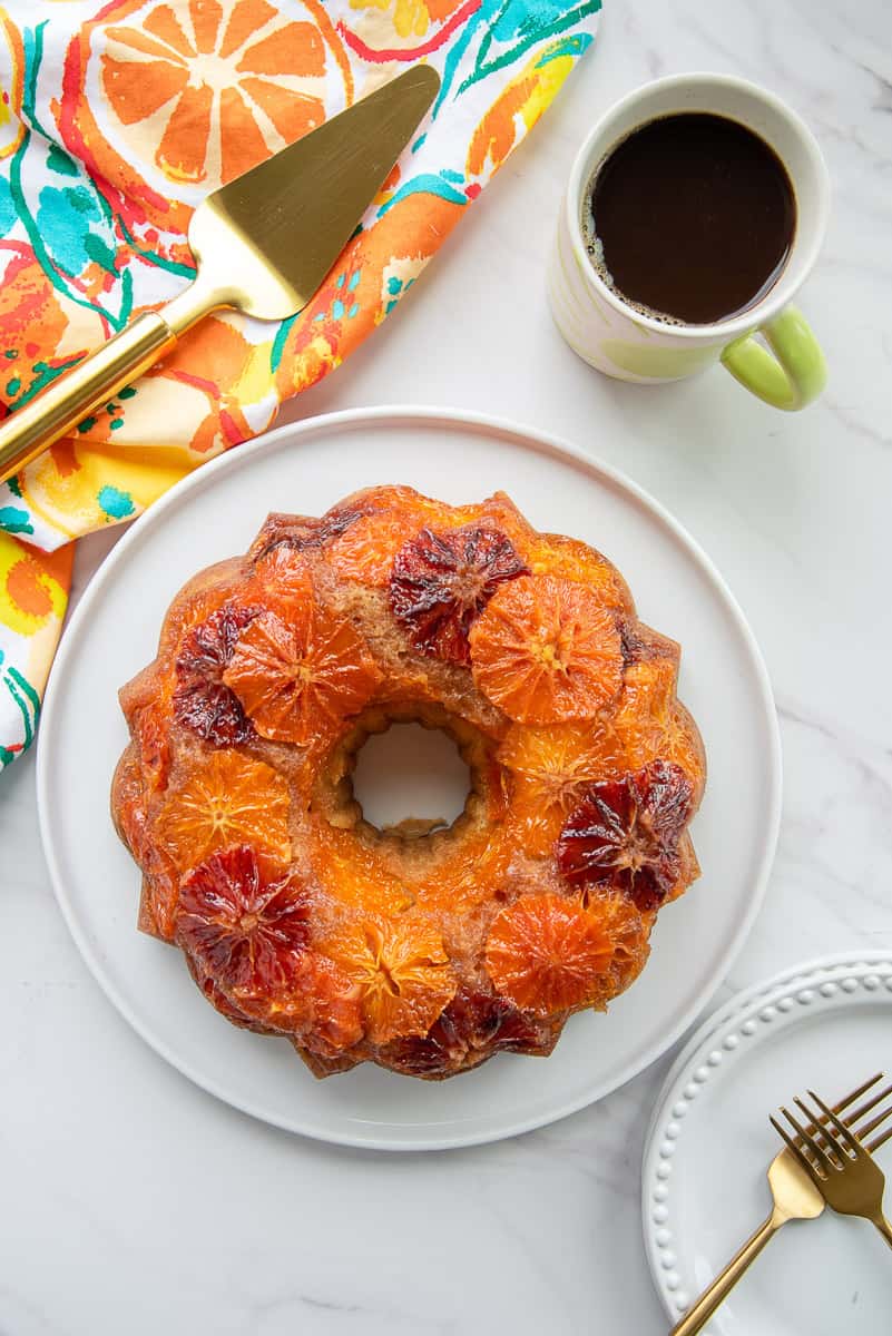 The top view of a Orange Ginger Coffee Cake next to a mug of black coffee and a colorful kitchen towel.
