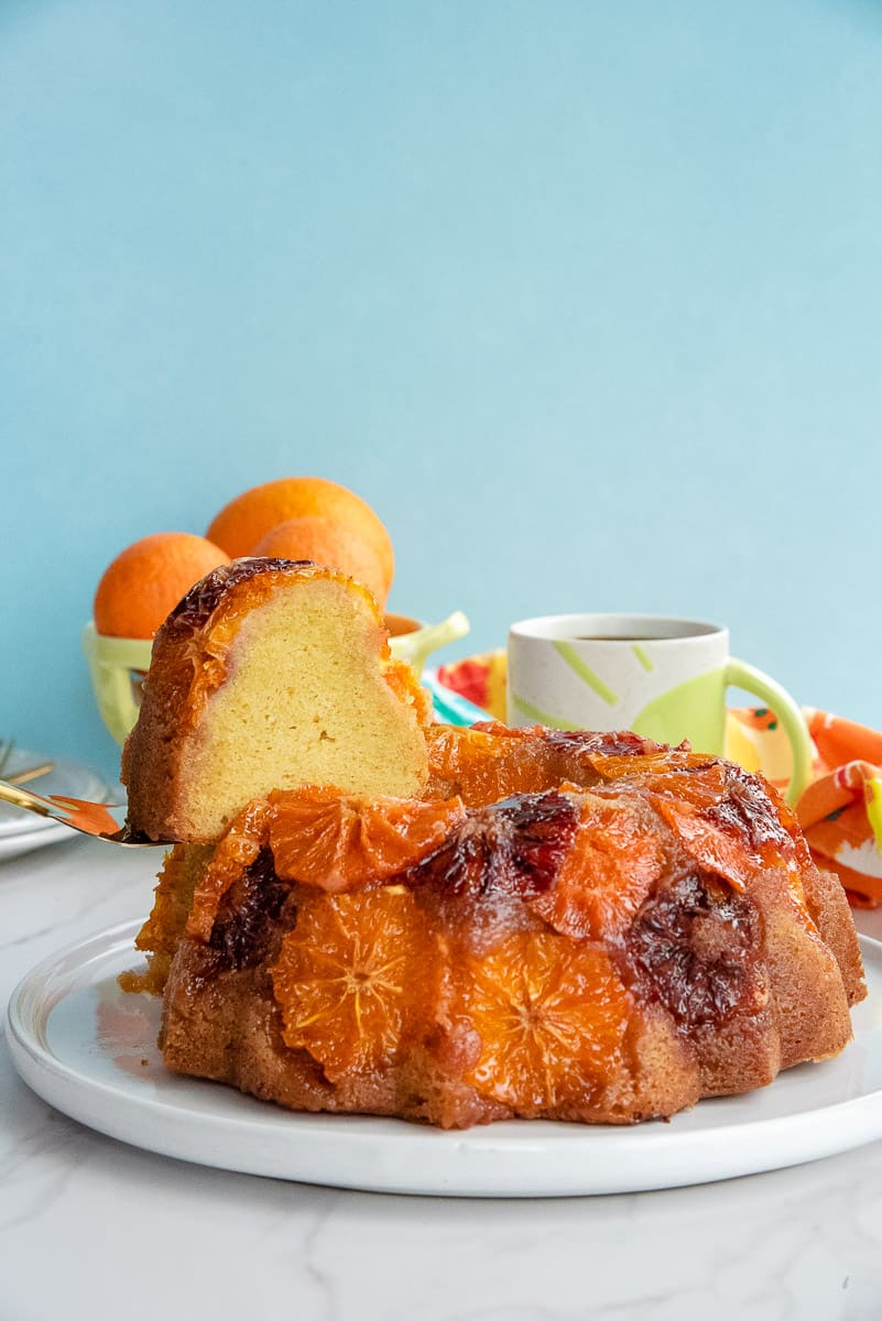 A slice of Orange Ginger Coffee Cake is lifted from the cake on a white serving plate.