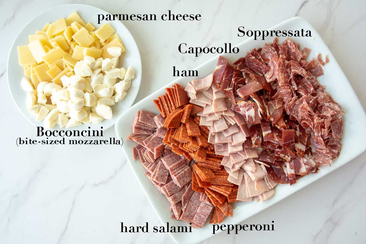 Different cheeses and cold cuts on a white countertop.