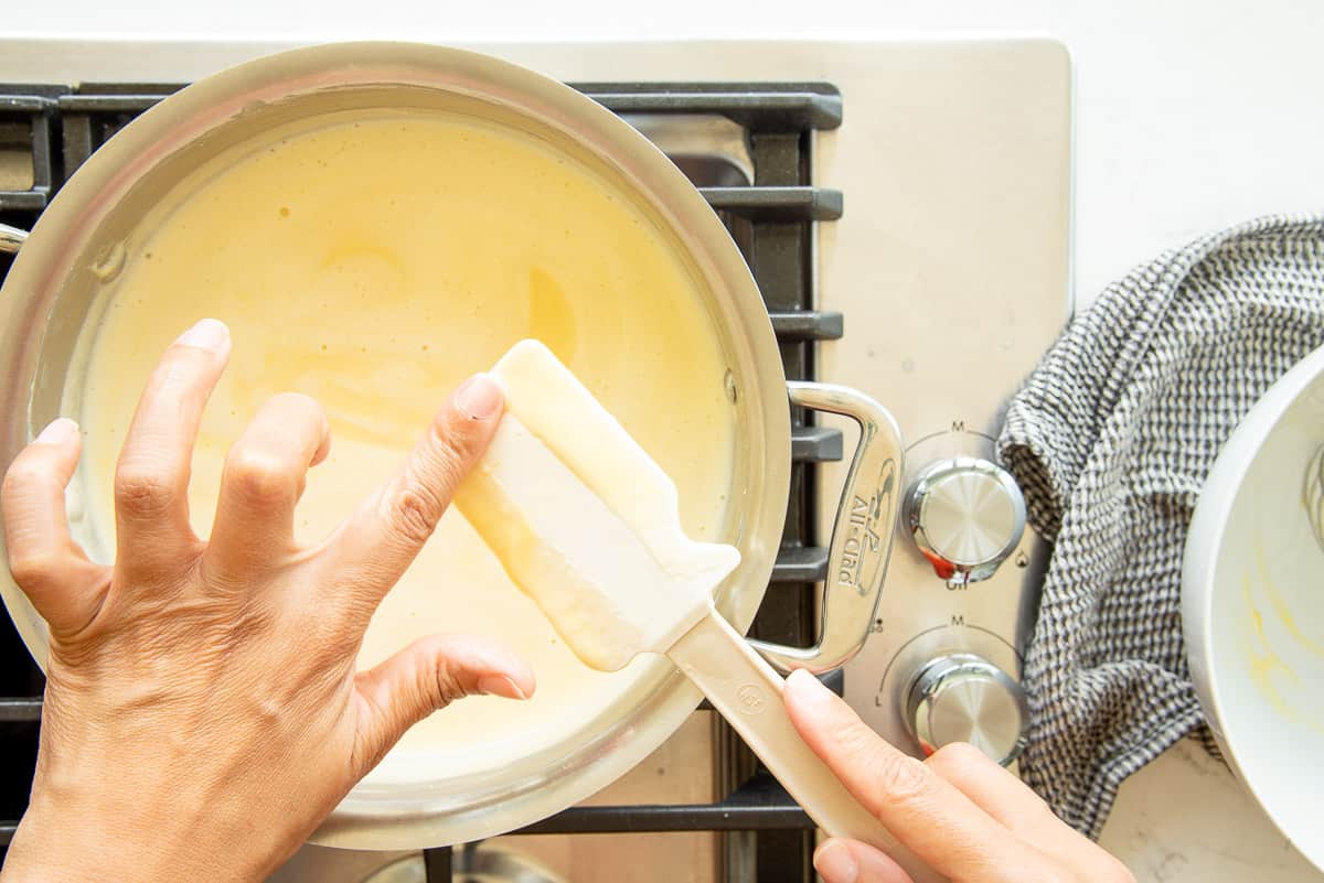 A hand uses a finger to check consistency of custard mixture.