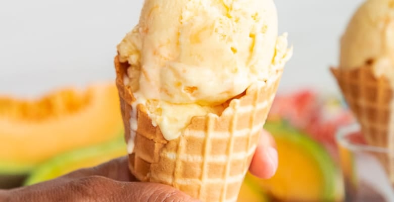 Hand holding a waffle cone filled with scoops of cantaloupe frozen custard.