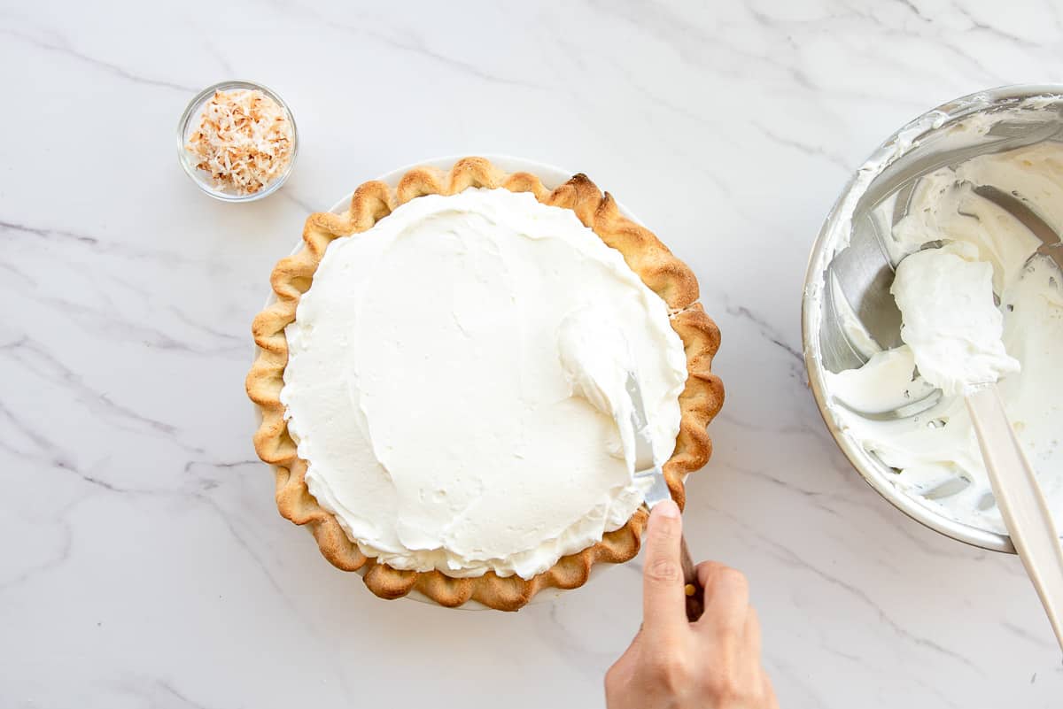 An offset spatula is used to smooth the whipped cream onto the pie.