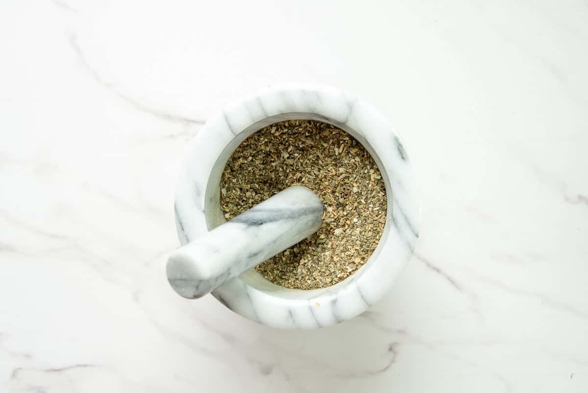 The Italian herb blend is ground in the mortar with a pestle.