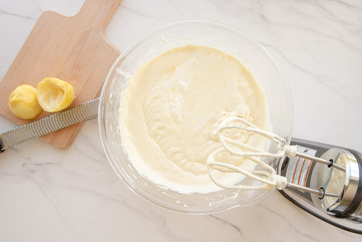The finished batter is mixed in a clear glass bowl by an electric hand mixer.