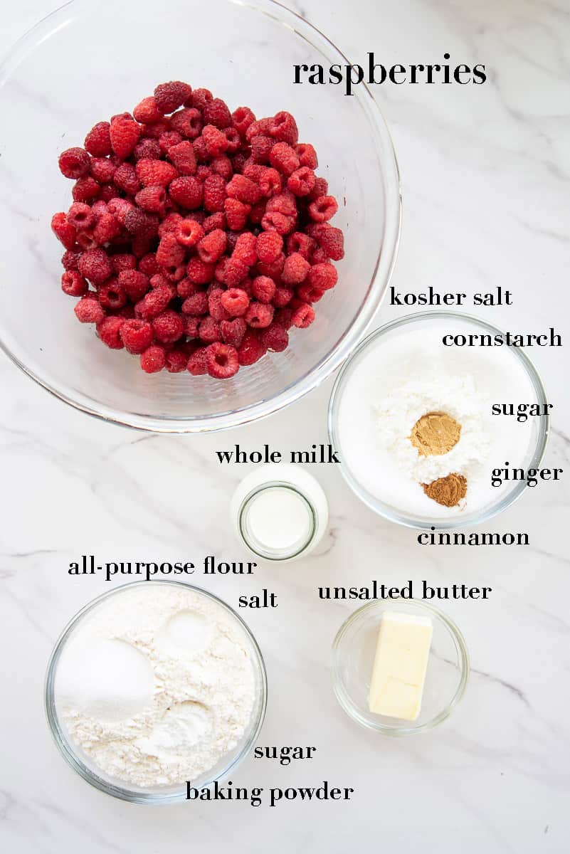 Ingredients needed to make raspberry cobbler on a white countertop labeled with black text.