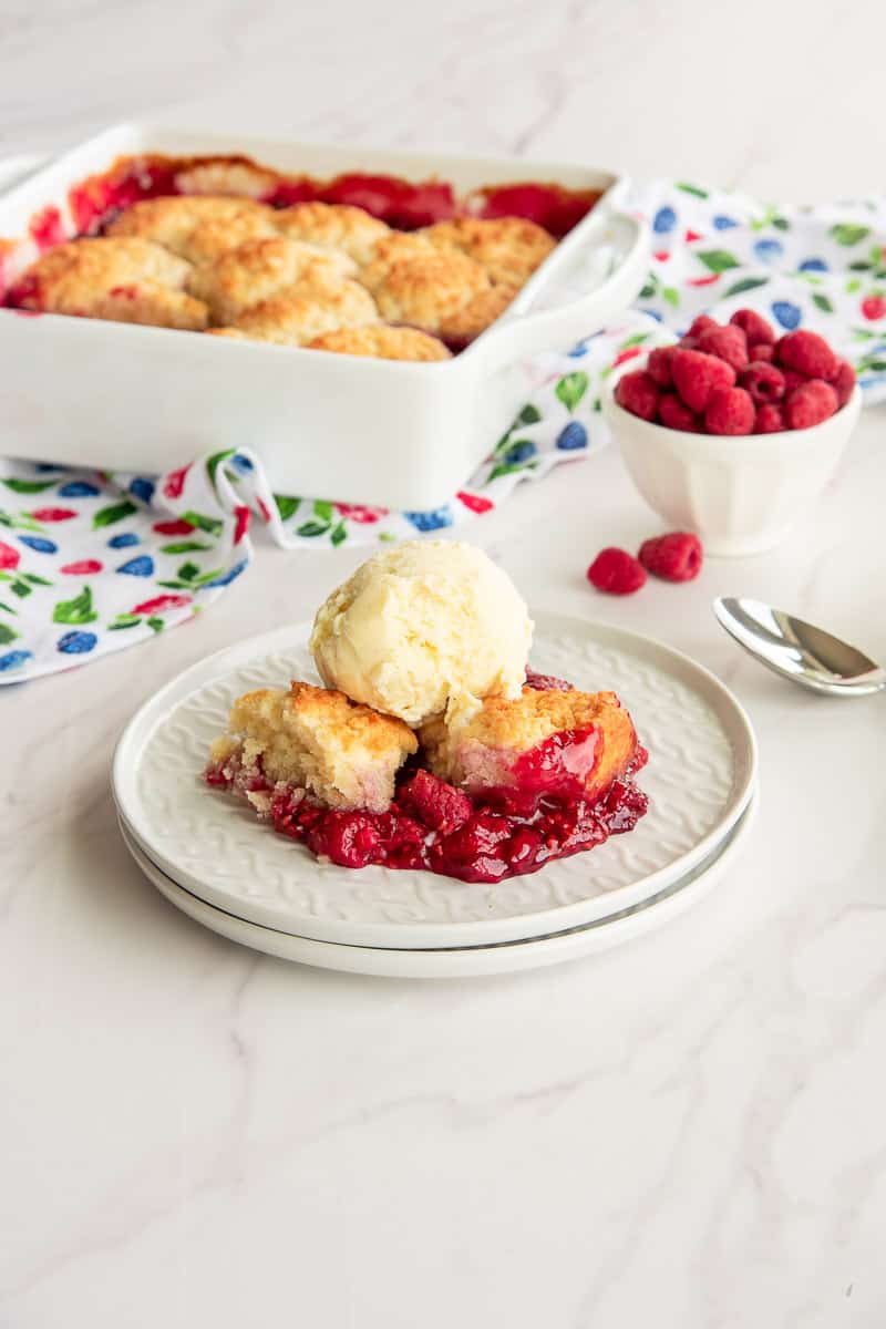 A serving of raspberry cobbler on a white plate with a scoop of vanilla Frozen Custard on top.