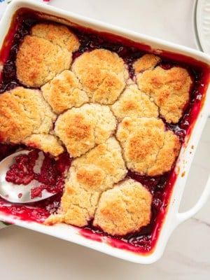 Raspberry cobbler and a white square ceramic baking dish with a serving scooped out.