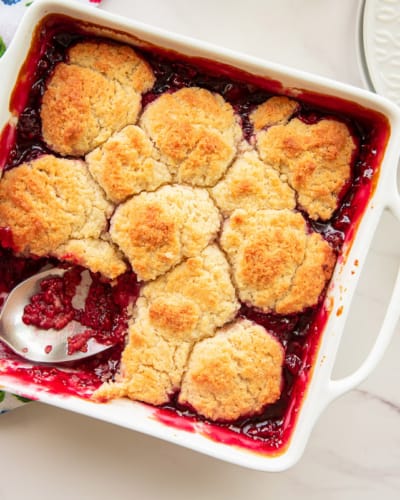 Raspberry cobbler and a white square ceramic baking dish with a serving scooped out.