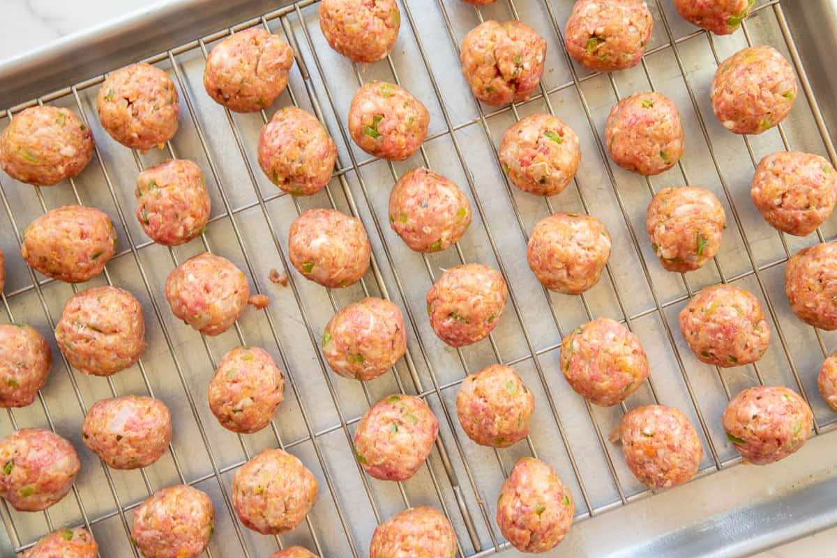 The meatballs on a cooling rack placed over a sheet pan before baking.