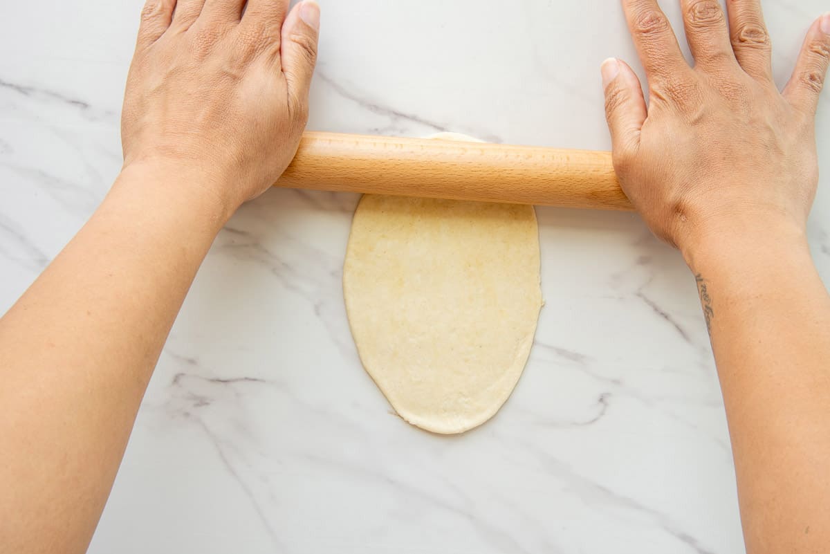 Two hands using a rolling pin to roll the dough into a disc.