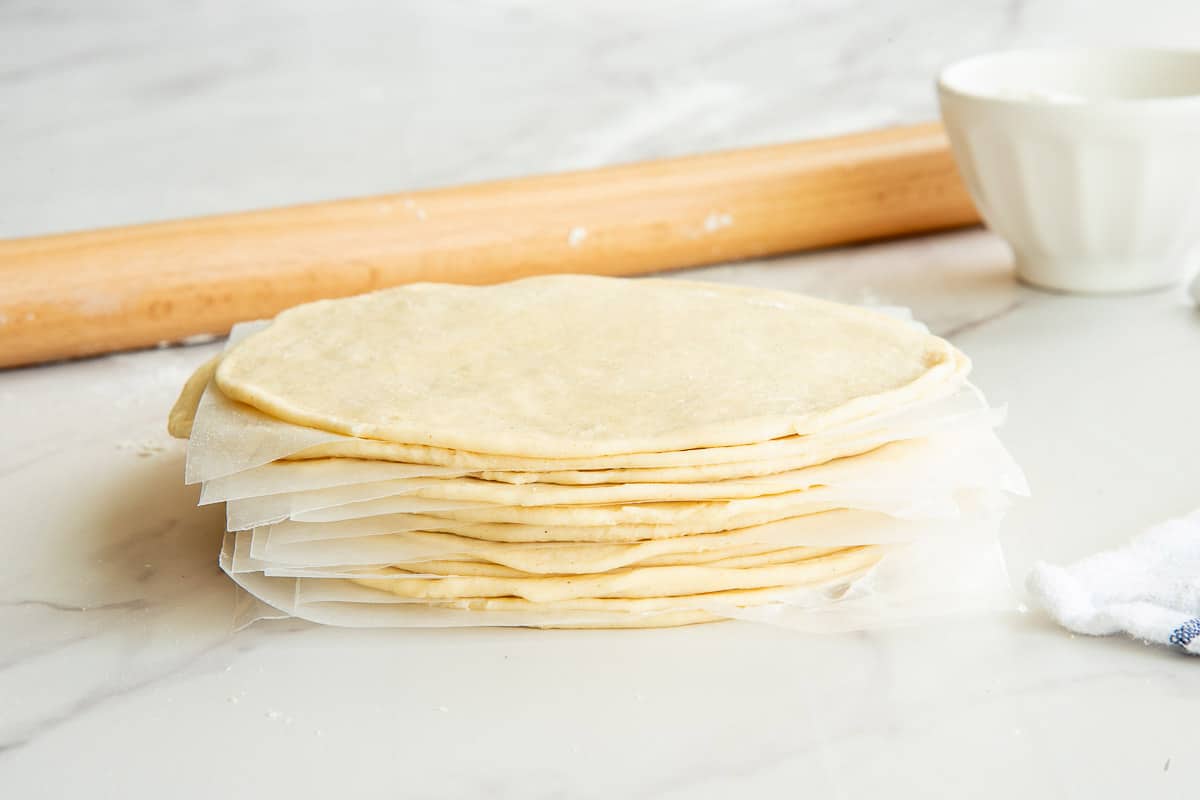 The empanada discs are stacked in front of a rolling pin and a white bowl.