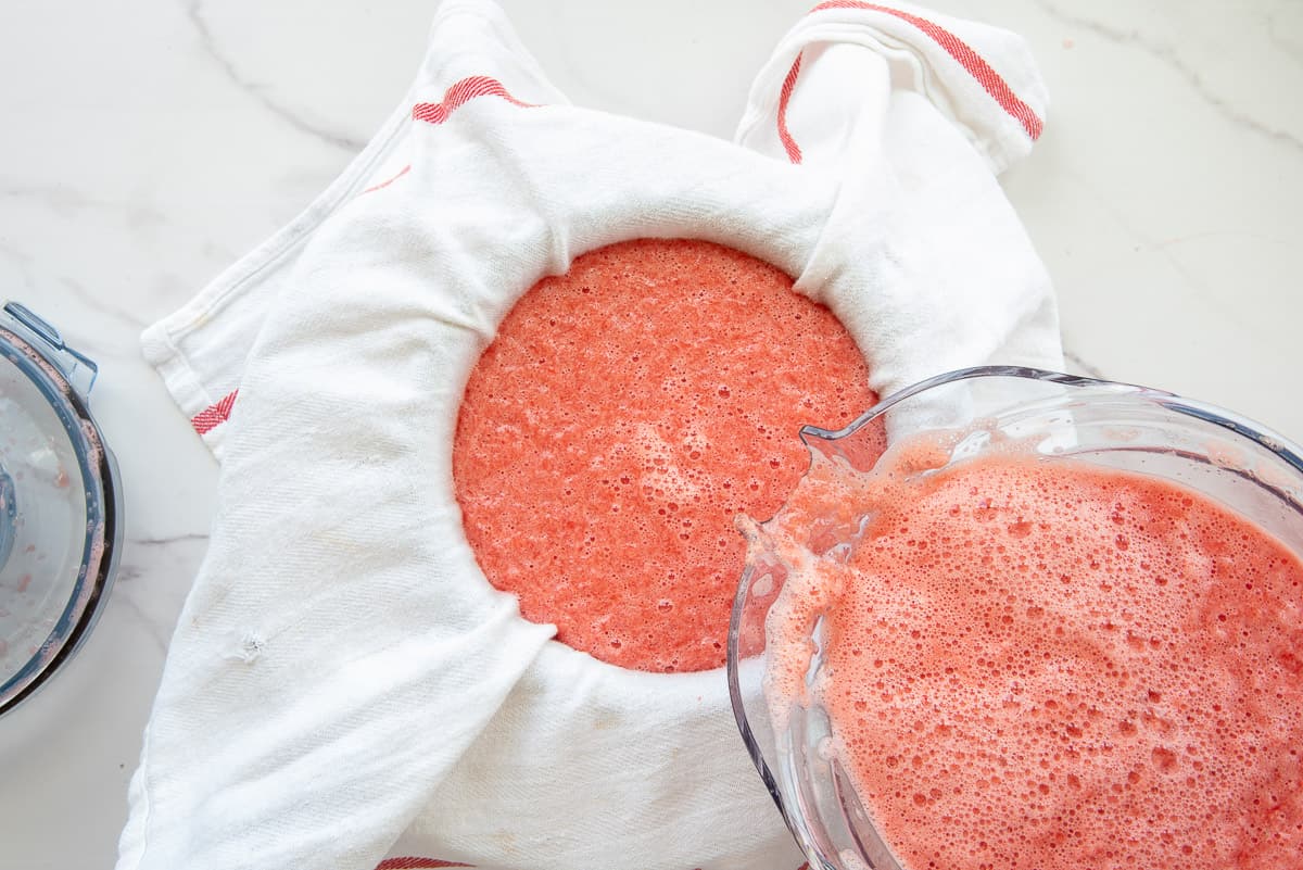 The pureed watermelon is poured into a white kitchen towel to be strained.