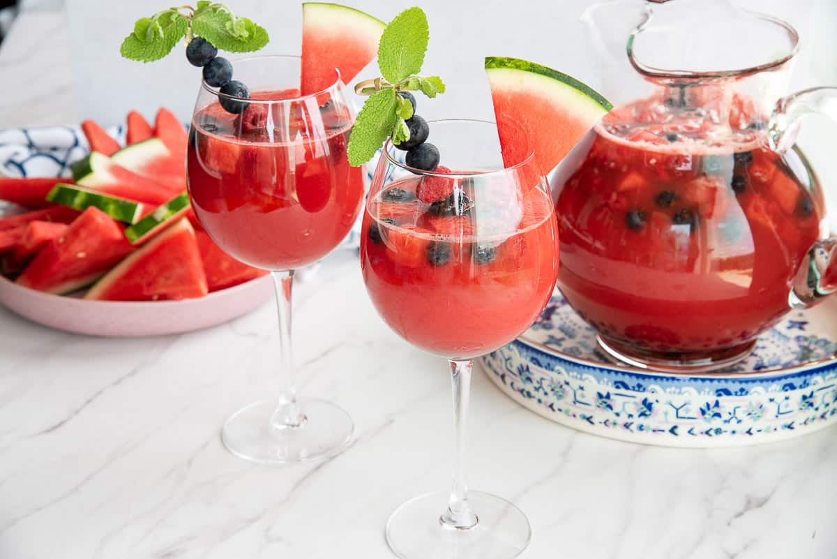 Two wine glasses filled with watermelon sangria garnished with fresh fruit in front of a pink bowl of watermelon slices.