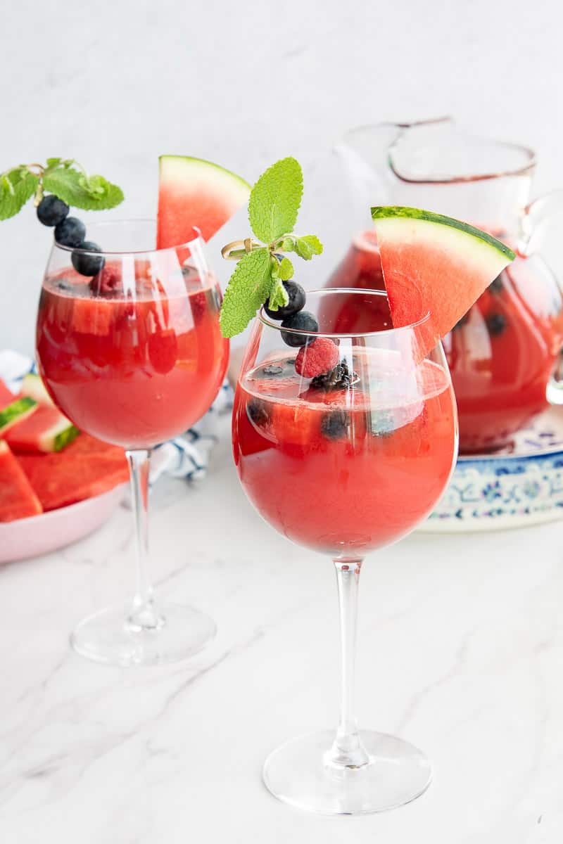 Two wine glasses filled with watermelon sangria garnish with a skewer of berries and a watermelon slice.