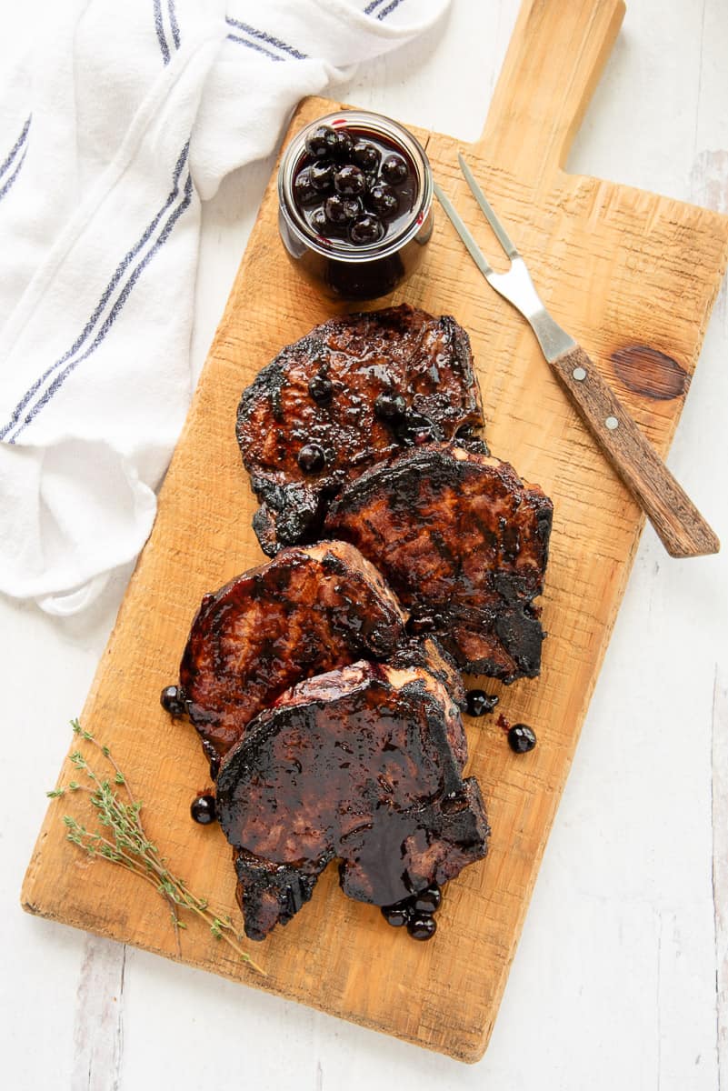 The Grilled Thick-Cut Pork Chops on a wooden board with a glass jar of BBQ sauce.