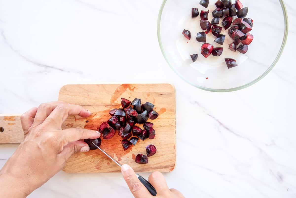 Hands use a paring knife to cut pitted cherries into eighths.