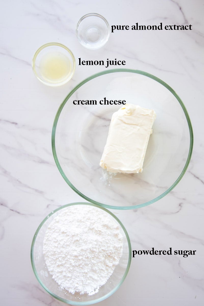 The ingredients to make the almond cream cheese icing are labeled on a white countertop.