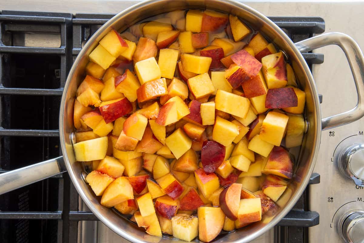 The cut peaches are simmered with water and ginger simple syrup in a wide pan on the stove.