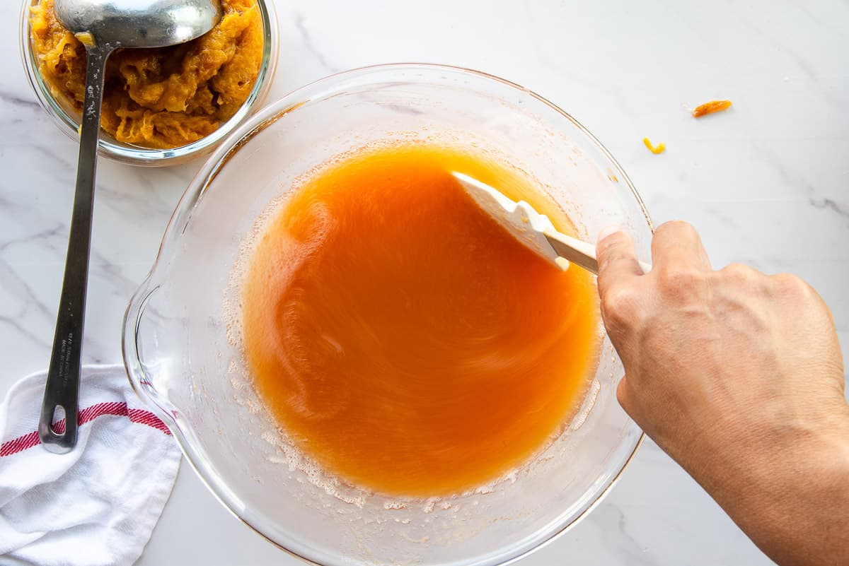 A hand stirs the fruit pulp in a glass mixing bowl.