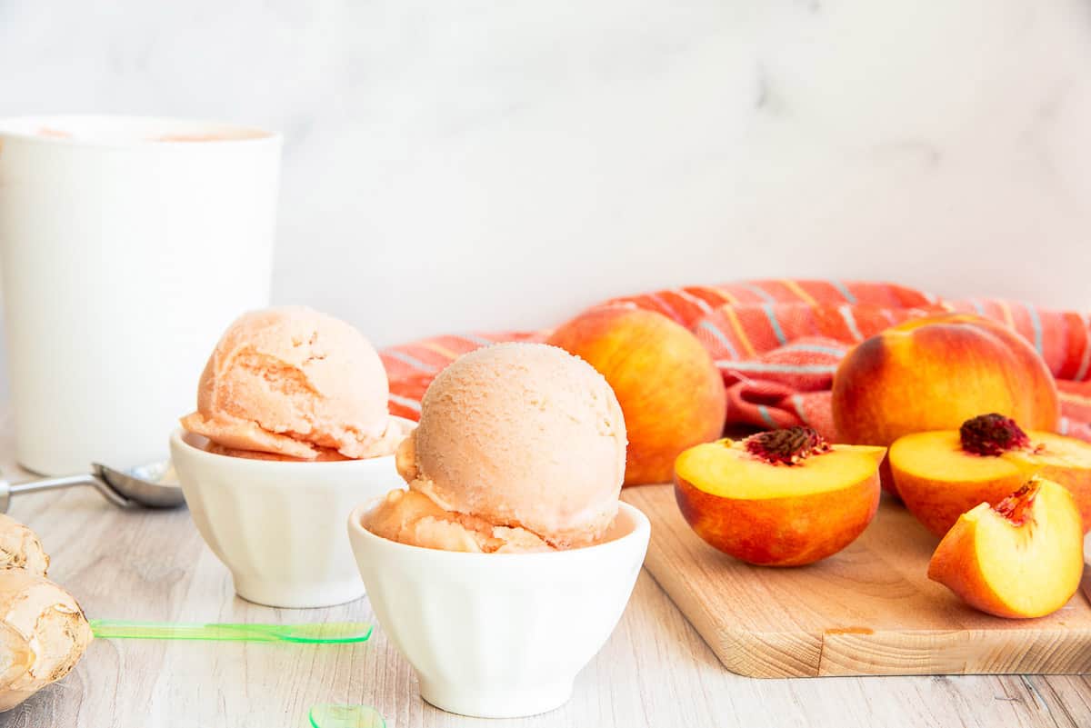 The Peach Sorbet in two white bowls next to a cutting board with peaches on it.