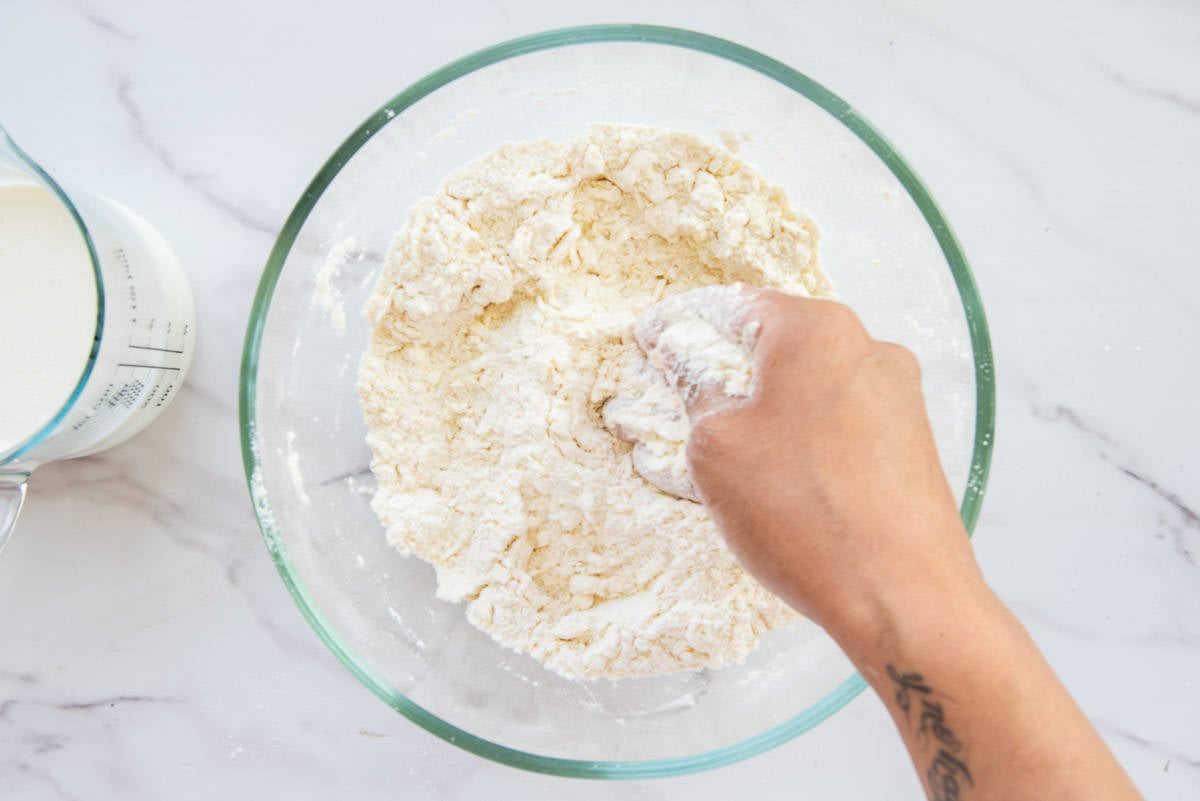 A hand cuts the cold butter into the all-purpose flour mixture.