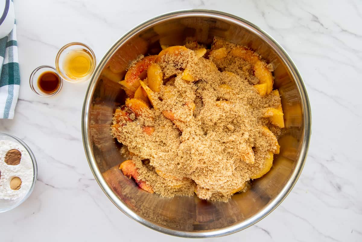 The brown sugar is added to the peaches in a larger silver mixing bowl so they can macerate.