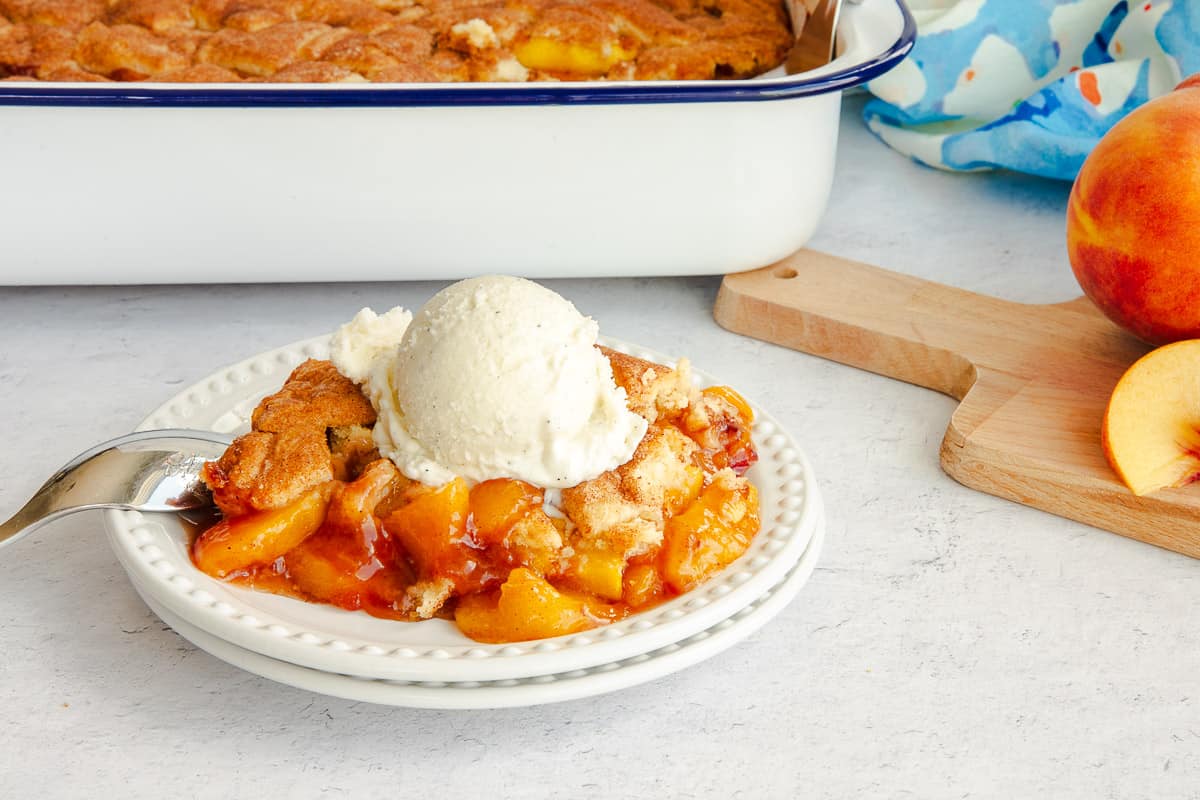 Homemade Peach Cobbler on a white plate topped with vanilla ice cream.