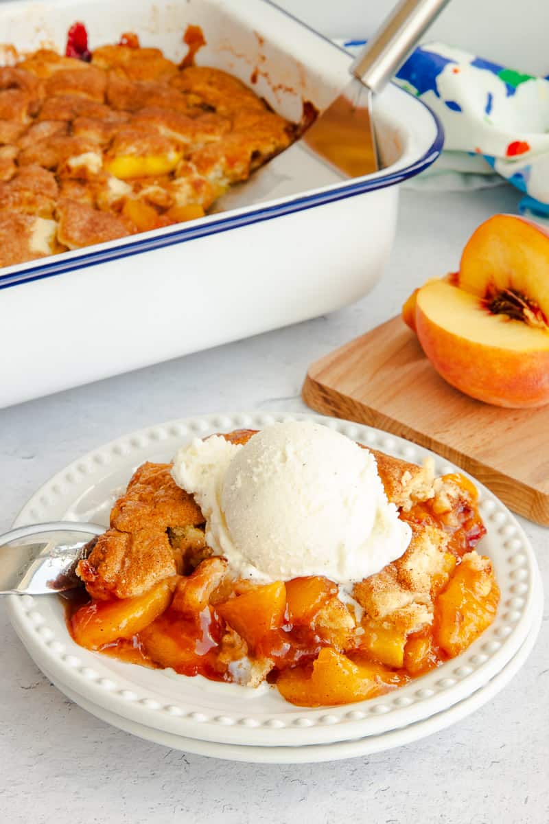A serving of Homemade Peach Cobbler on a white plate served a la mode style.