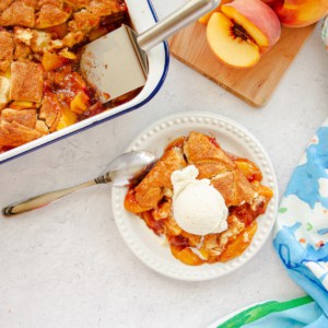 A serving of Homemade Peach Cobbler on a white plate topped with vanilla ice cream.