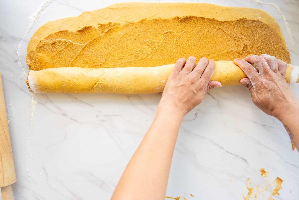 Two hands roll up the the dough into a tube shape.