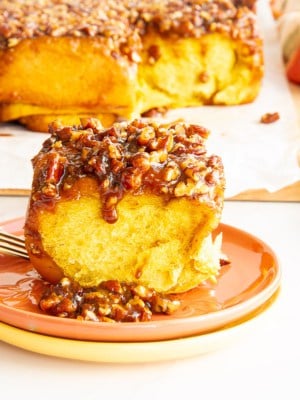 A Pumpkin Sticky Bun on a stack of fall-colored plates in front of a board with the Pumpkin Sticky Buns on it.