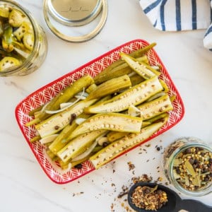 Spicy Pickled Okra on a small red and white platter next to a blue and white striped kitchen towel.