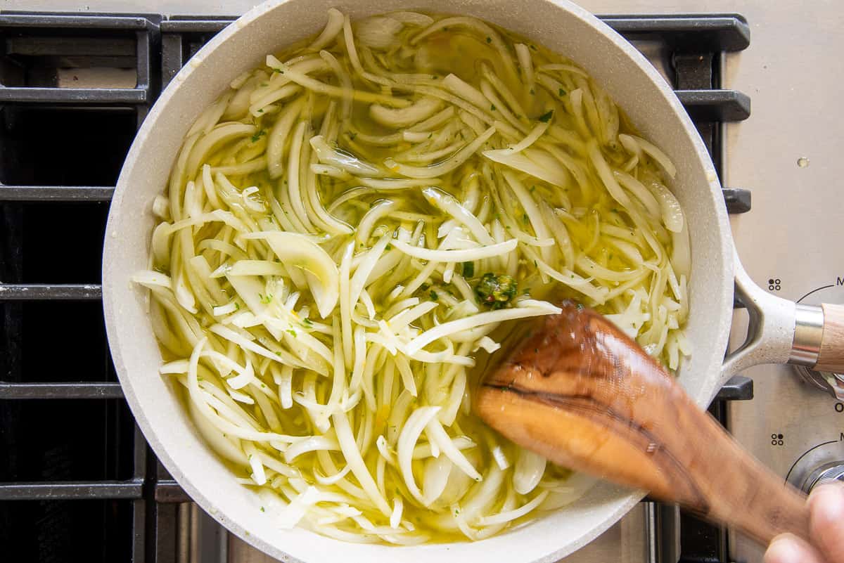 The onions, garlic, and sofrito are added to the pan of oil to slowly heat.