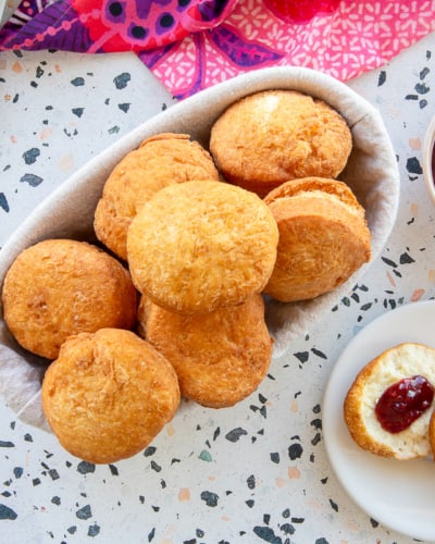Caribbean Johnny Cakes in a bread basket next to a bowl of jam and a plate with a Johnny cake split in half, topped with butter and jam.