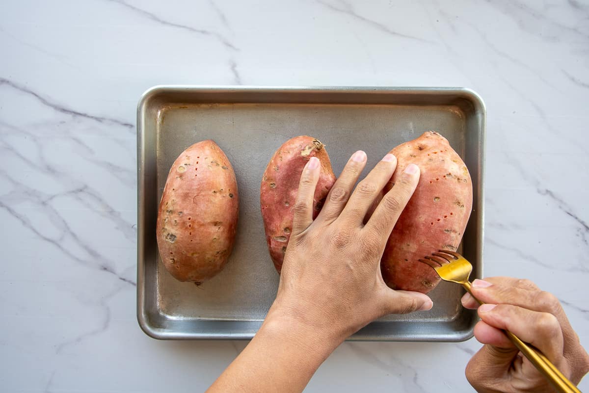 Hands hold a fork that is used to pierce the potatoes before they're roasted.