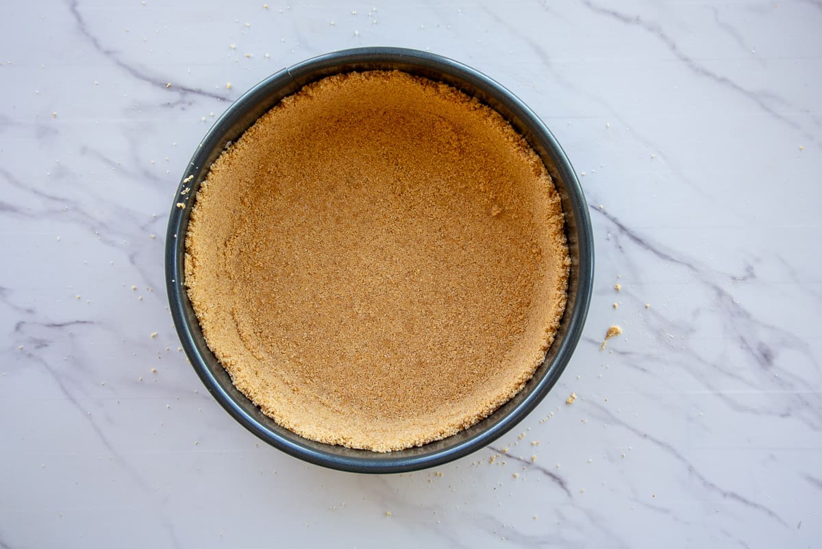 The graham cracker crust mixture is formed in a springform pan before baking.