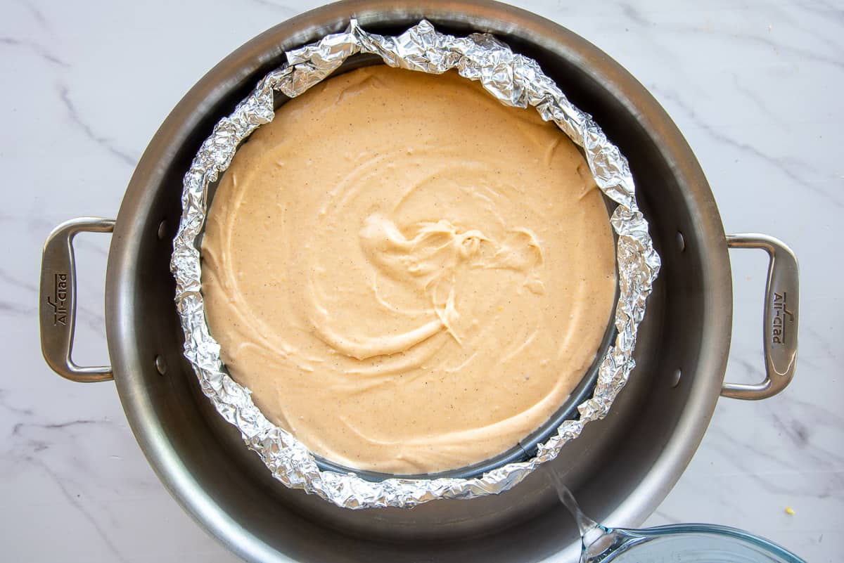 Boiling water is poured into an outer pan to create a water bath for baking the cheesecake in.