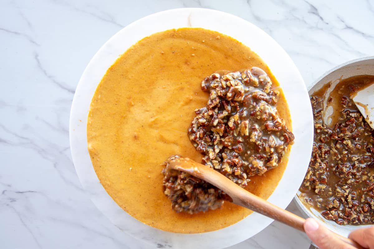A spoon is used to top the sweet potato cheesecake with the pecan praline topping.