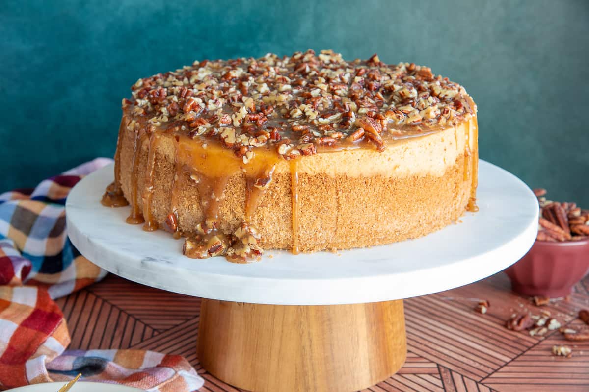 A whole Sweet Potato Cheesecake with Pecan Praline Topping on a marble cake stand with a wood base.