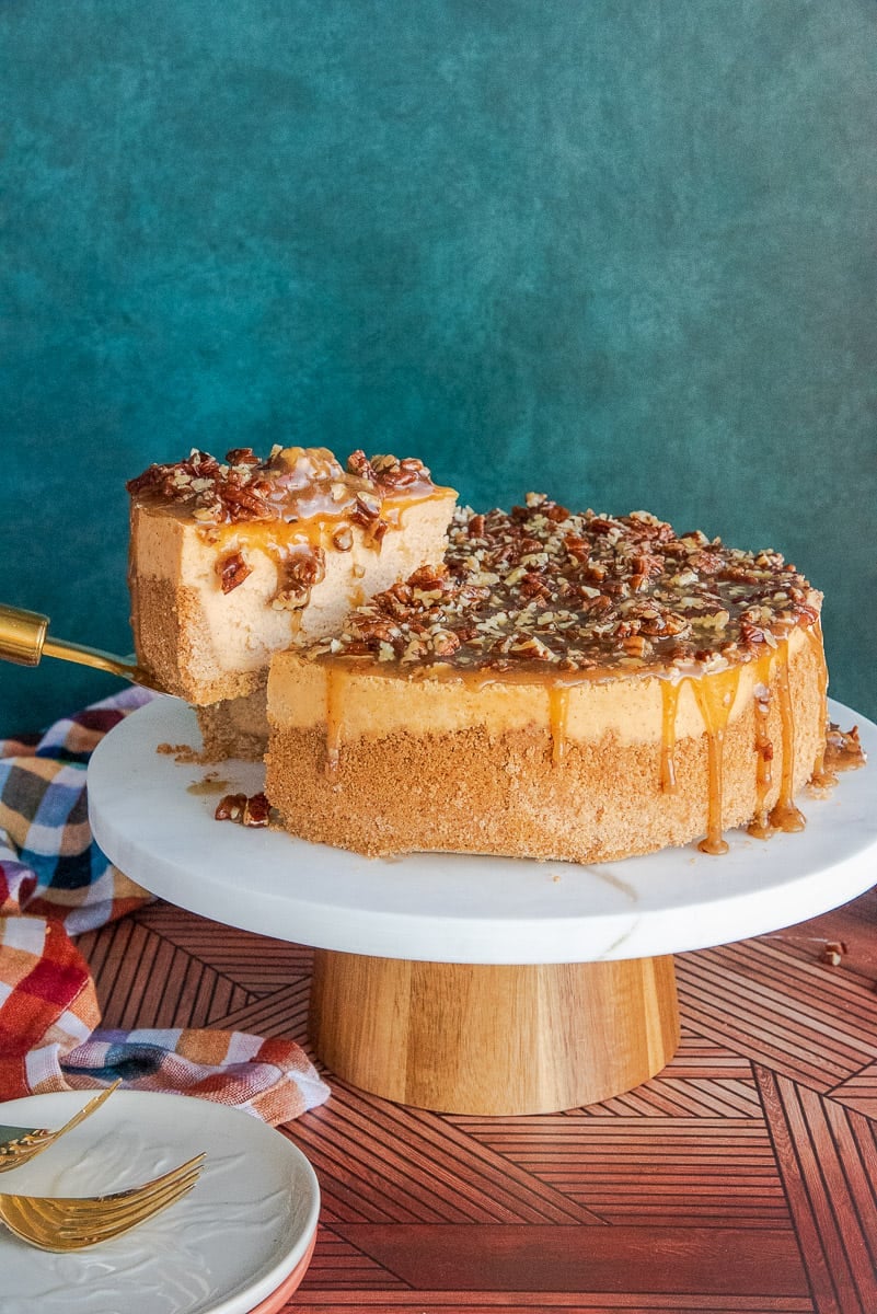 A serving of Sweet Potato Cheesecake with Pecan Praline Topping is lifted from the rest of the cheesecake on a cake stand.