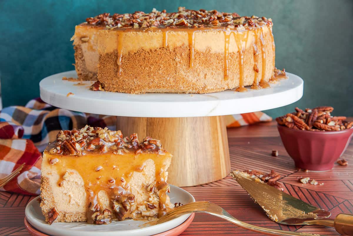 Sweet Potato Cheesecake with Pecan Praline Topping sliced on a beige plate in front of a cake stand with the cheesecake on it.