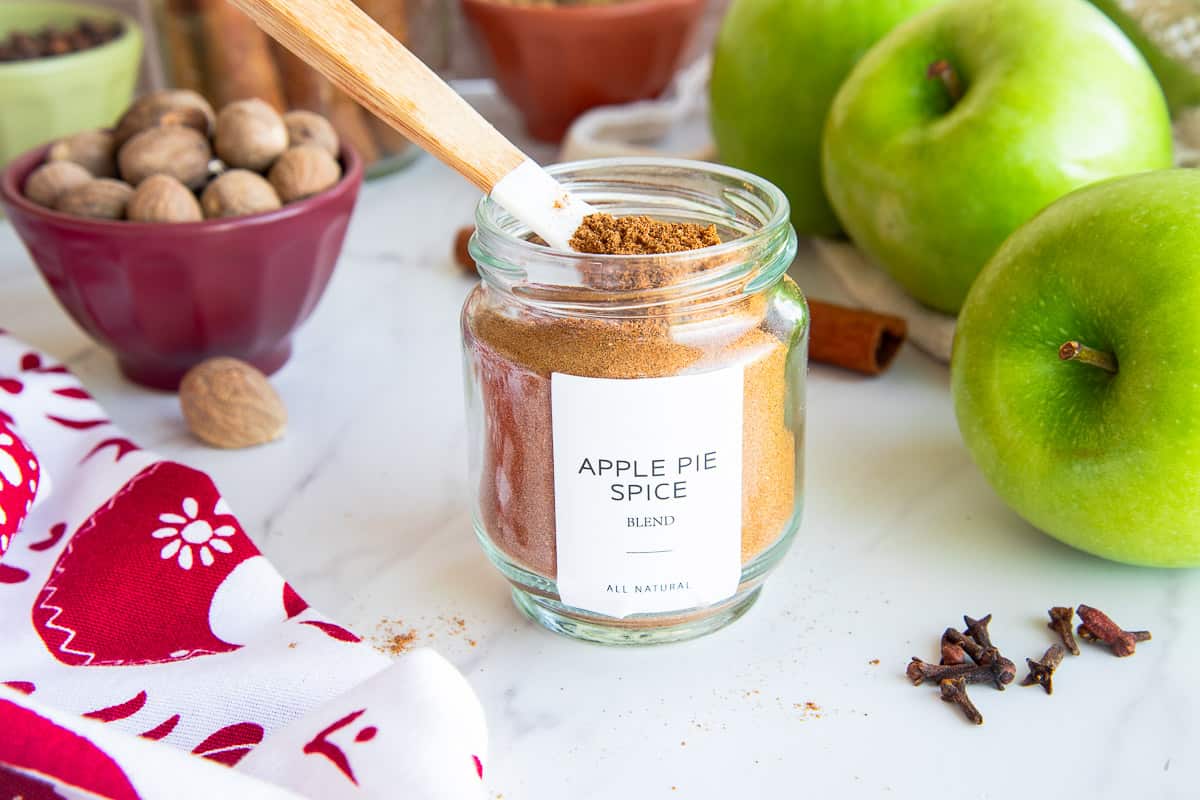 A glass jar of Apple Pie Spice Blend with a spoon in it.