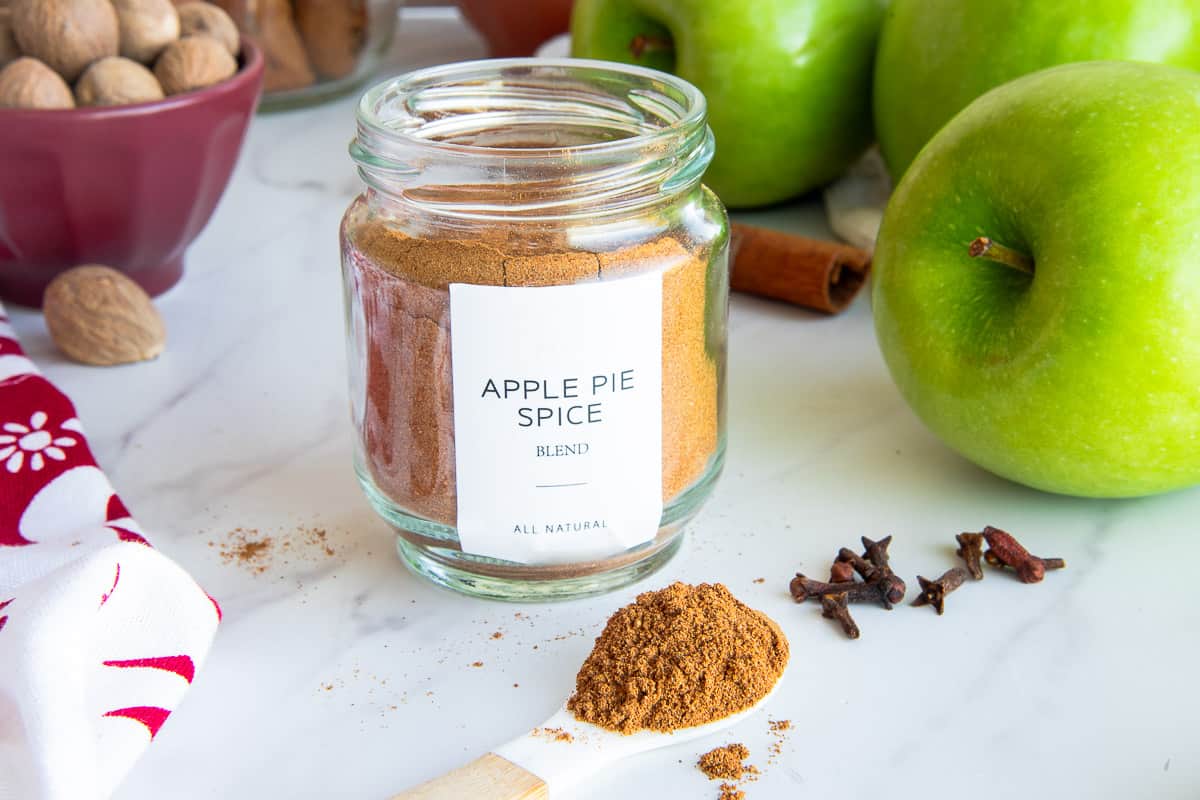A jar of Apple Pie Spice Blend with a white label that reads the contents. A spoonful of the spice blend sits in front of the jar.