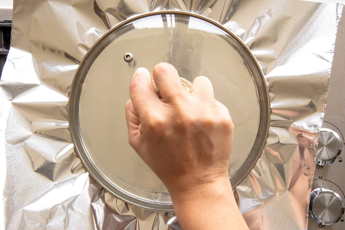 A hand places the lid on a piece of foil over the pot.