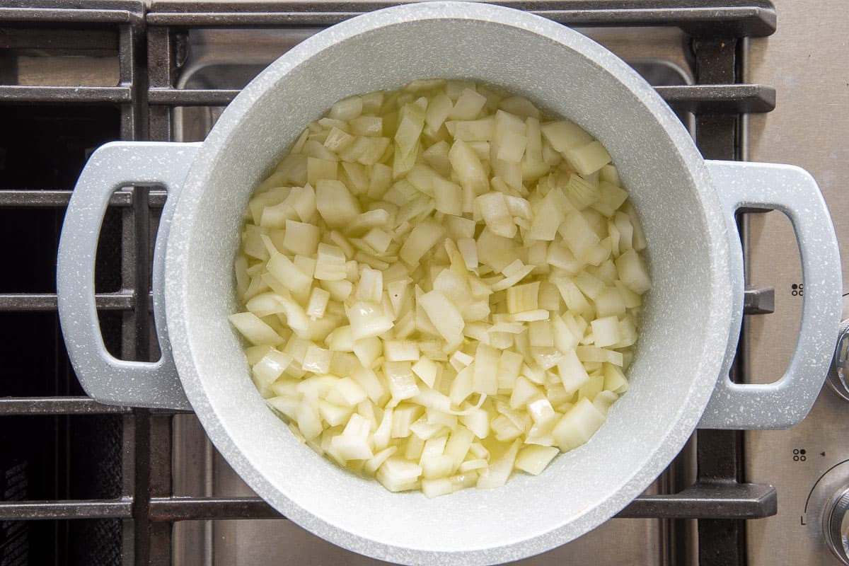 The onions are sautéed in olive oil in a blue-grey pot on the stovetop.